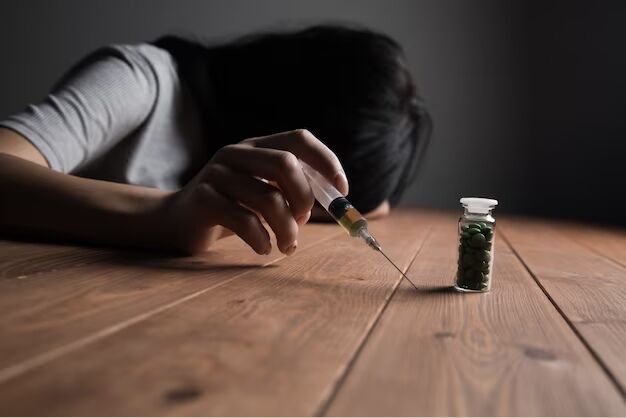Why Do People Become Addicted to Drugs – A person struggling with addiction, looking distressed, with pills and a syringe nearby.